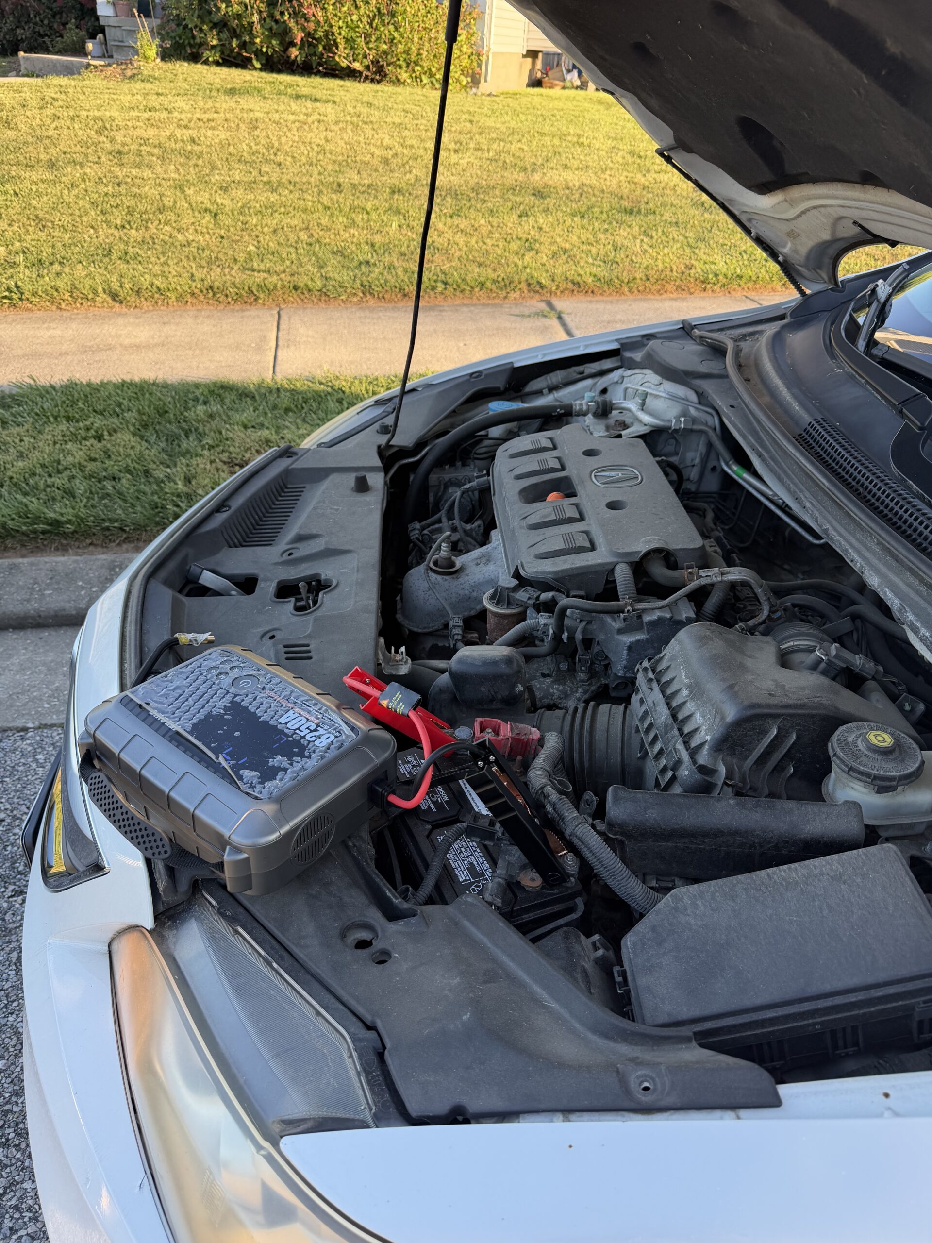 Portable jump starter beside the battery under the open hood of a white Acura ILX