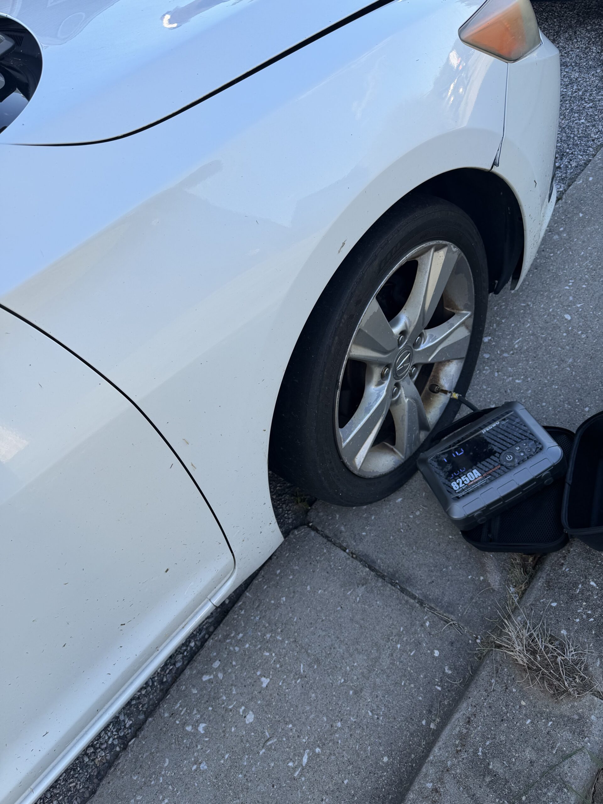 Portable tire inflator hose attached to the front tire valve on a white Acura ILX in Reisterstown