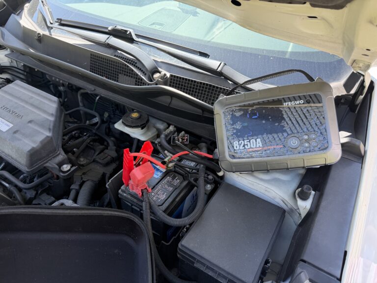 Portable jump starter and battery clamps under the open hood of a Honda CR-V in Reisterstown