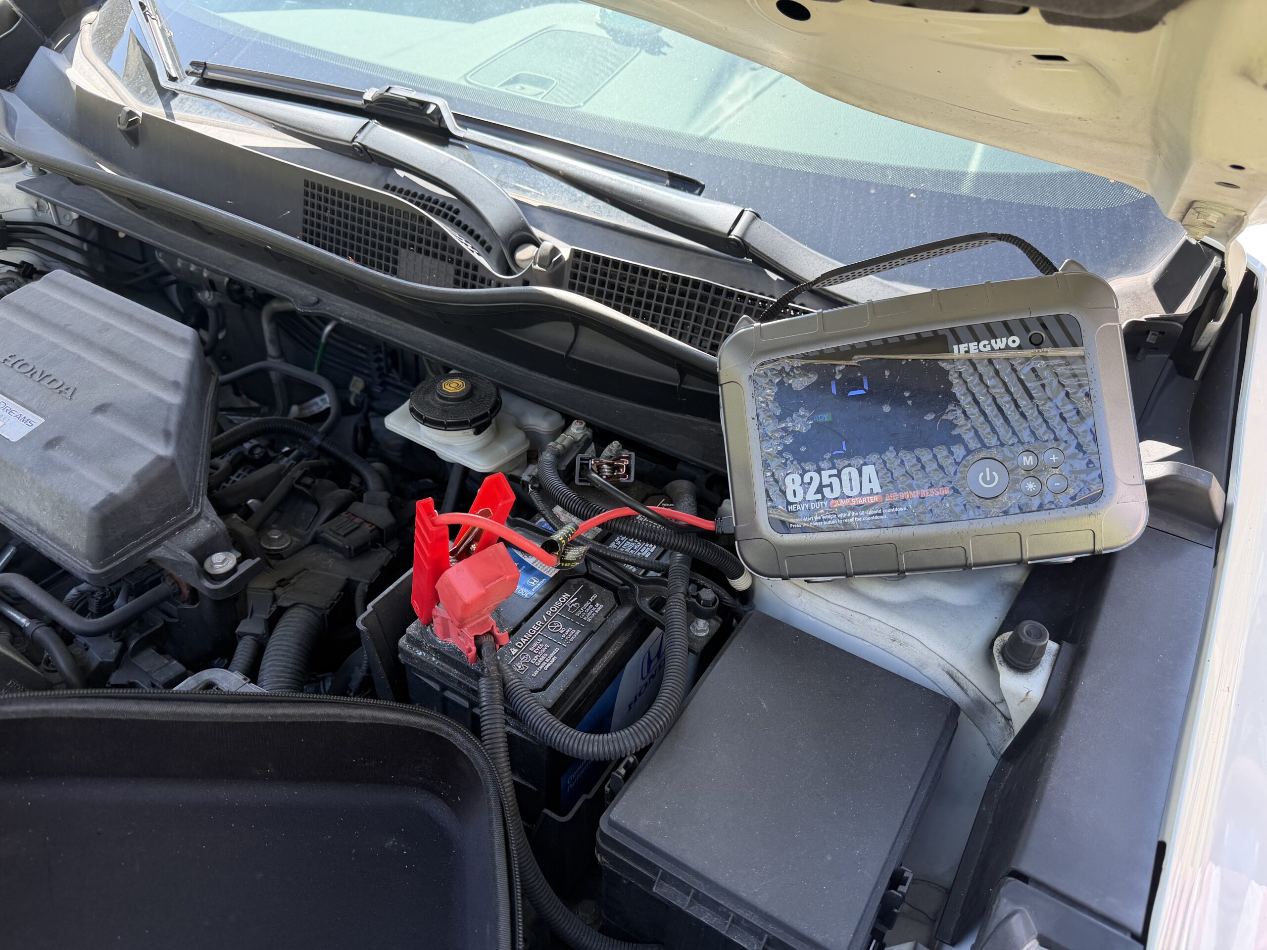 Portable jump starter and battery clamps under the open hood of a Honda CR-V in Reisterstown