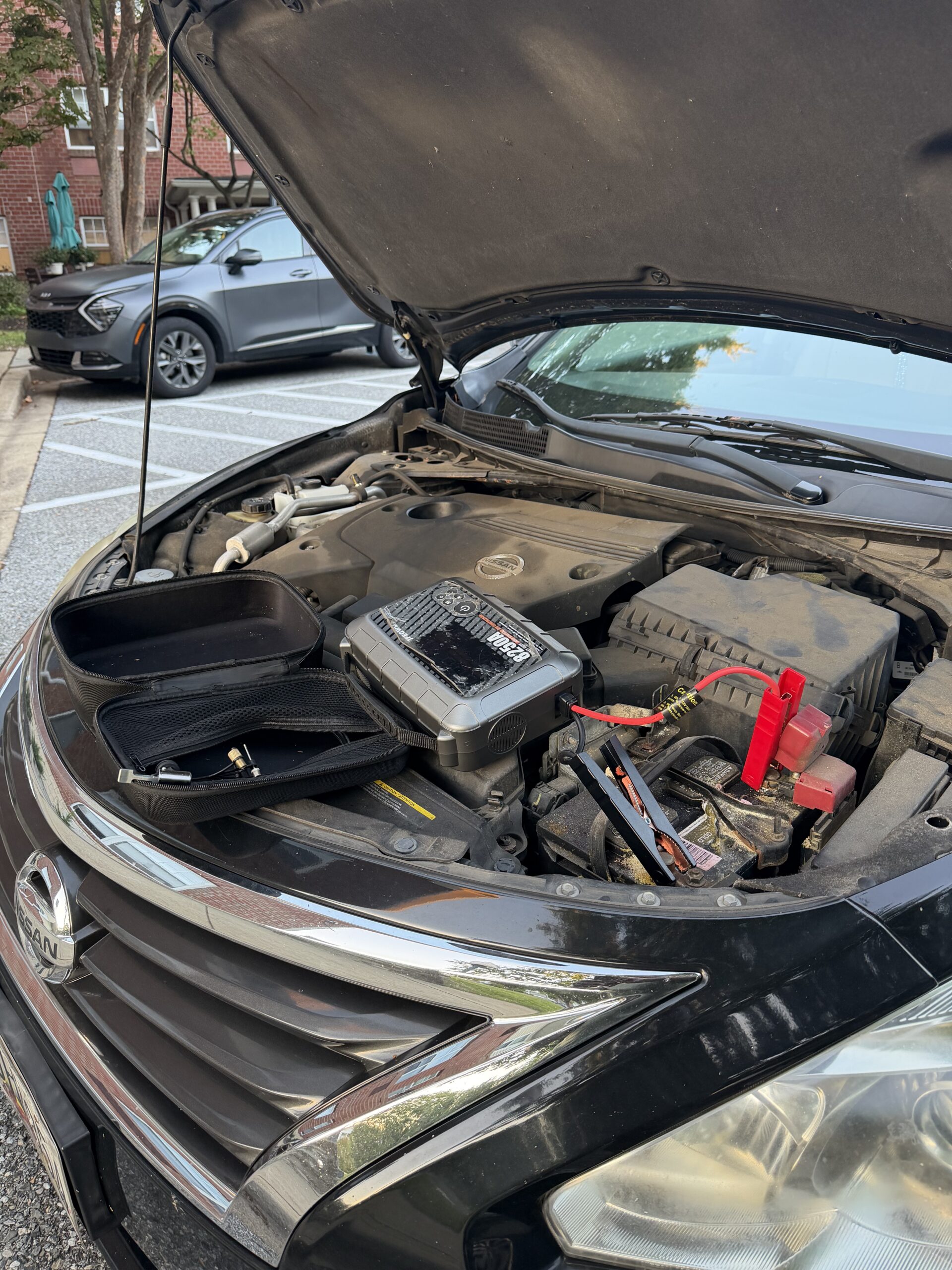 Front view of the Nissan Altima with its bonnet open and portable jump starter beside the battery in Reisterstown