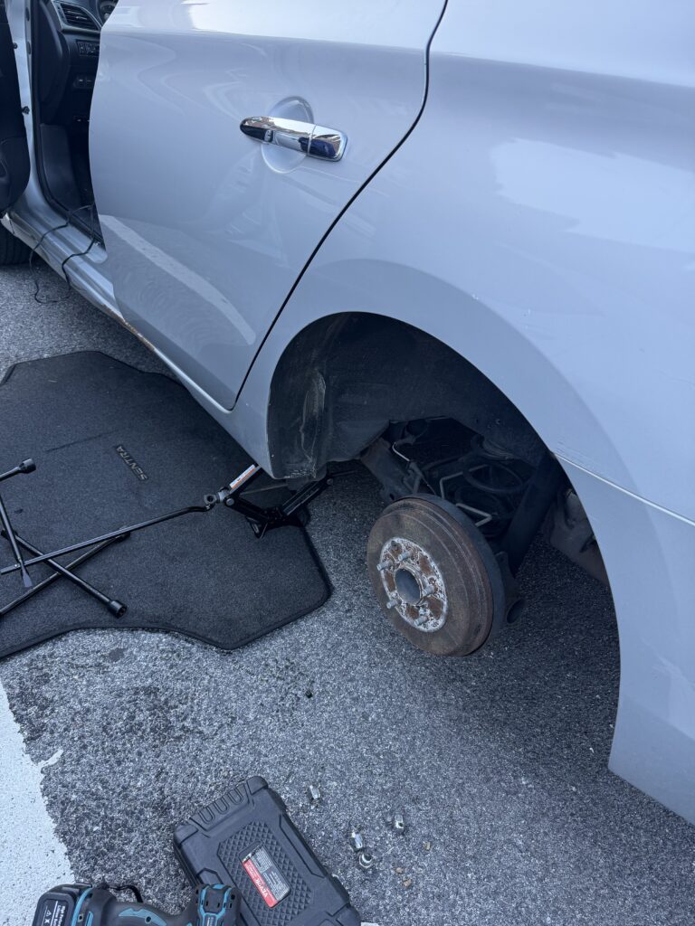 Removed rear wheel on a white Nissan with exposed wheel studs and wheel tools during the Reisterstown callout