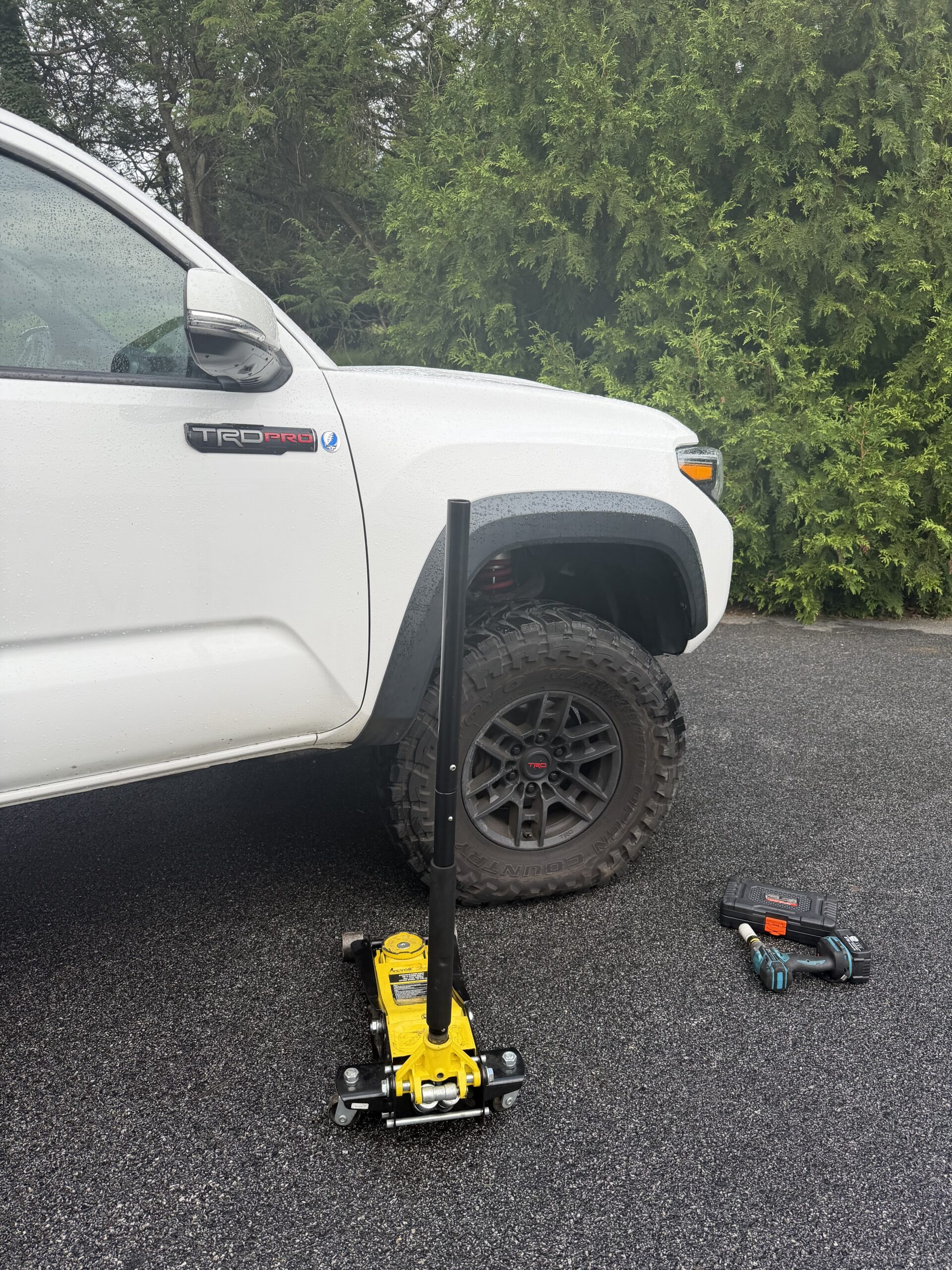 Toyota Tacoma with a large all-terrain tire beside a yellow floor jack and cordless impact wrench in Garrison