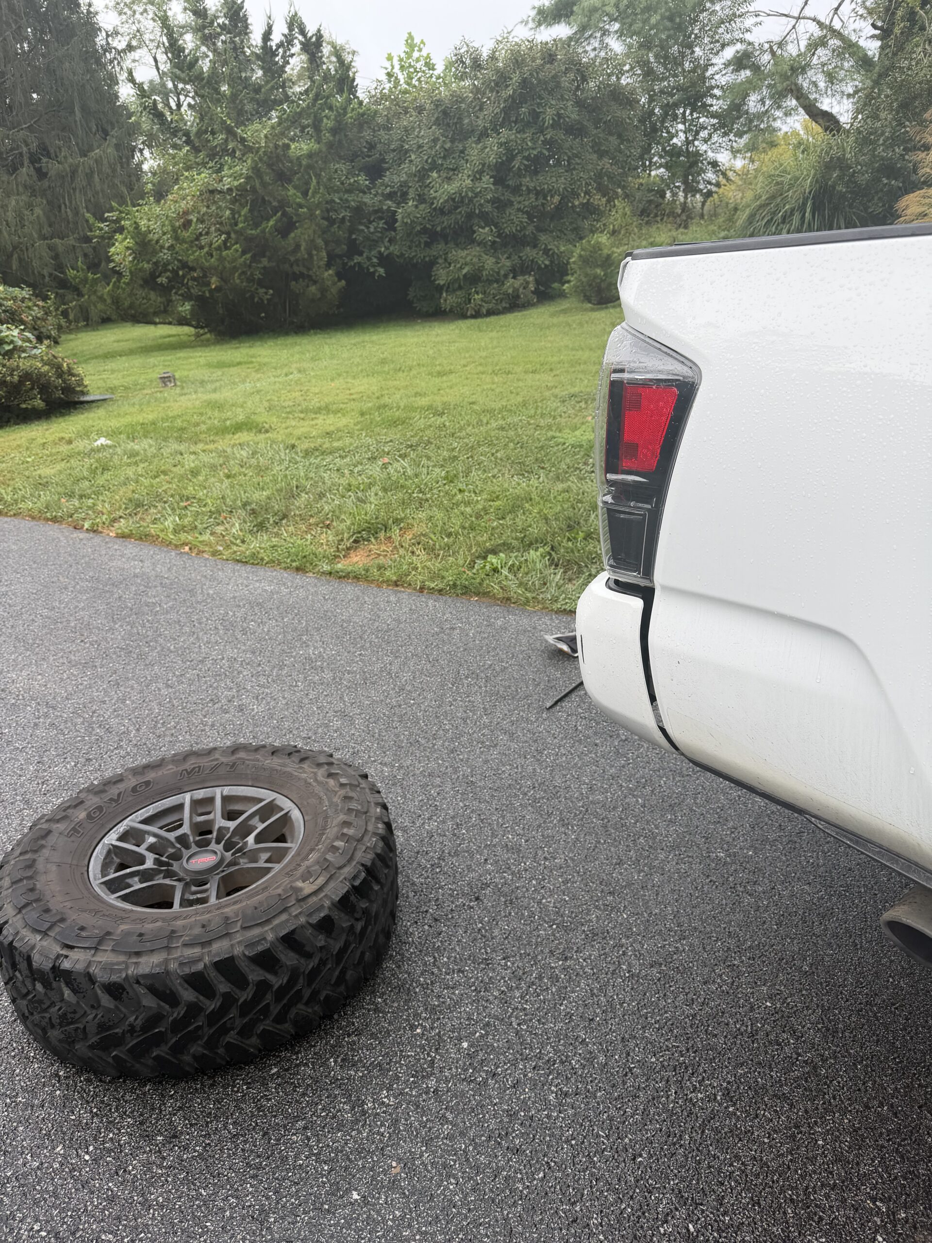 Removed all-terrain tire and alloy wheel beside the rear of the Toyota Tacoma during its Garrison tire change